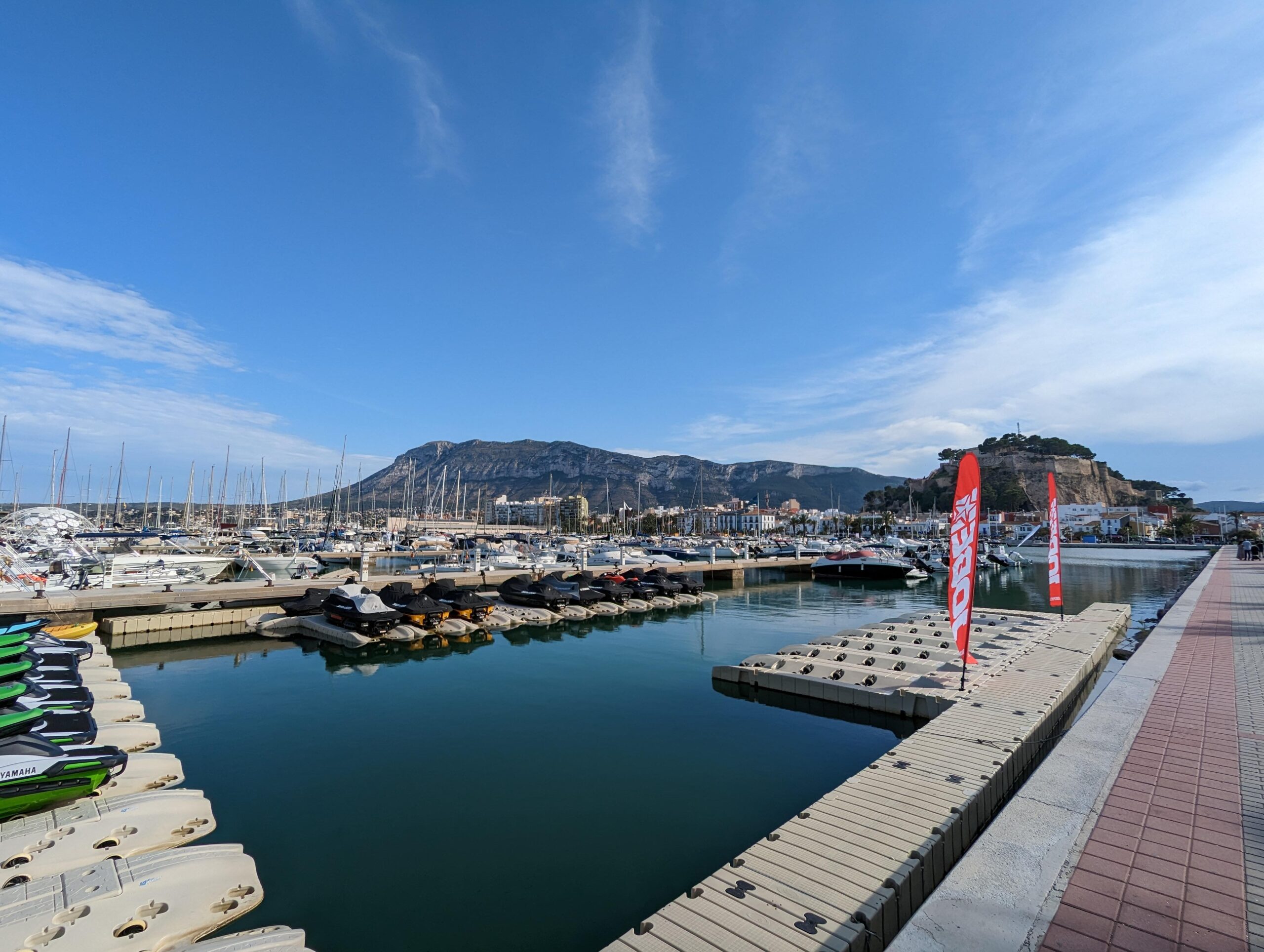 Blick auf den Yachthafen mit Jetskis und Yachten vor einer Bergkulisse.