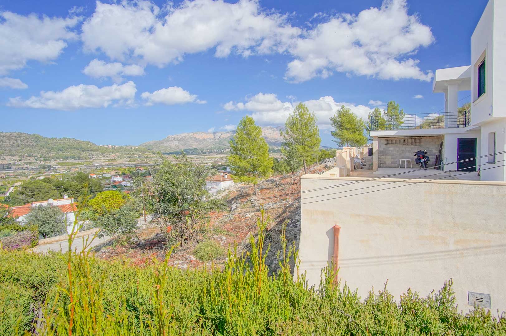 Außenansicht der Villa mit Terrasse und Stellplatz, die einen weiten Panoramablick über das Tal und die markante Berglandschaft bietet.