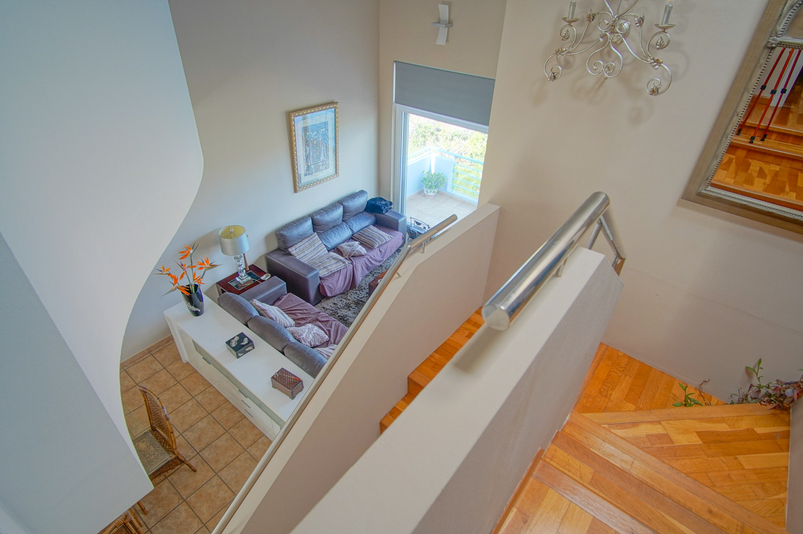 Blick von oben auf die Holztreppe mit Edelstahlgeländer und das Wohnzimmer mit doppelter Deckenhöhe und direktem Zugang zur Außenterrasse.