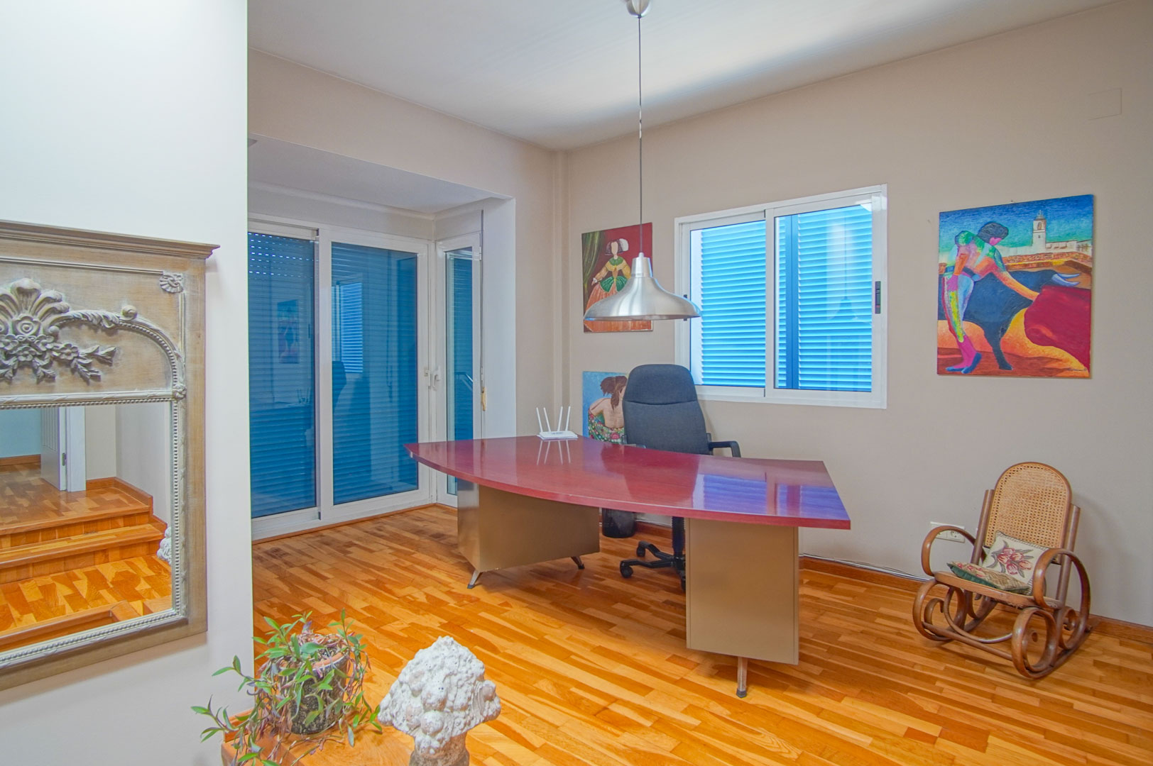 Helles Arbeitszimmer mit Parkettboden, einem großen geschwungenen burgunderroten Schreibtisch und Fenstern mit traditionellen blauen Fensterläden.