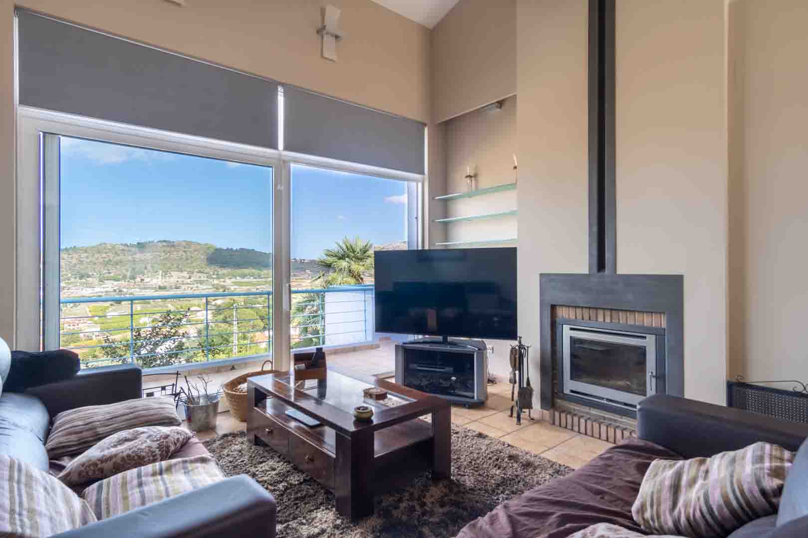Helles Wohnzimmer mit Einbaukamin, Terrakottaboden und bodentiefen Fenstern, die einen Panoramablick auf das Tal und die Berge bieten.