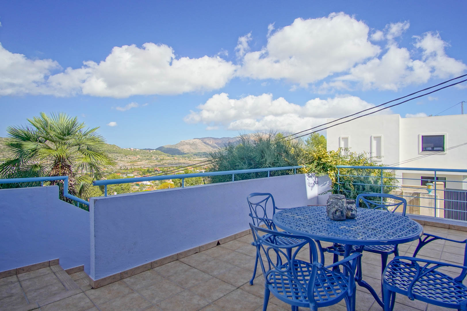 Hochterrasse mit blauen Schmiedeeisenmöbeln, Fliesenboden und Panoramablick auf das Tal und die Berge von Pedreguer.