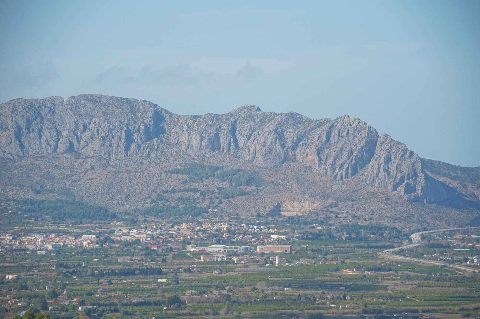 Panoramablick auf das zerklüftete Gebirge und das Tal, der die strategische Lage nahe der Autobahn und die mediterrane Umgebung verdeutlicht.