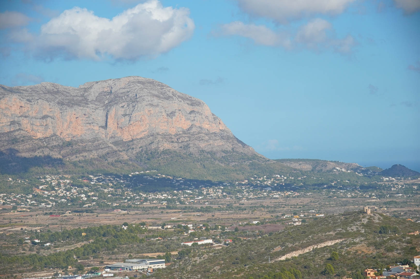Panoramablick vom Anwesen auf das Montgó-Massiv, das weite Tal und den Horizont des Mittelmeers unter einem leicht bewölkten Himmel.