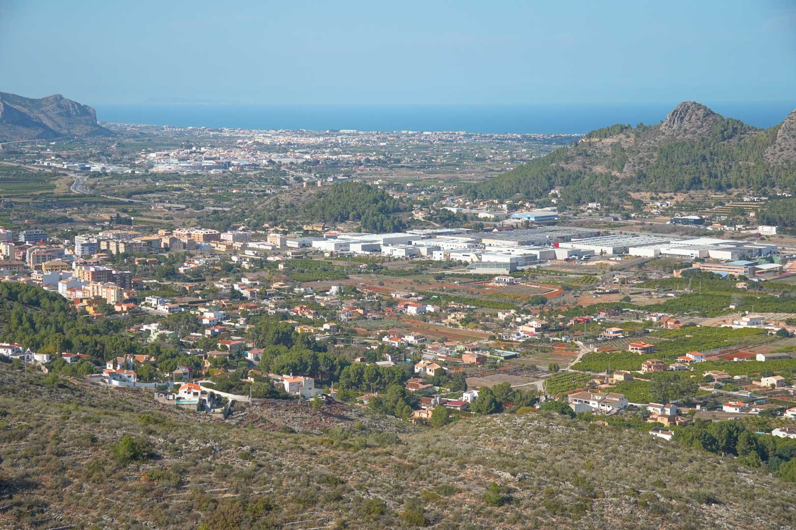 Panoramablick vom Anwesen über das Tal von Pedreguer, mit Blick auf die Stadtlandschaft und das Mittelmeer am Horizont unter klarem Himmel.