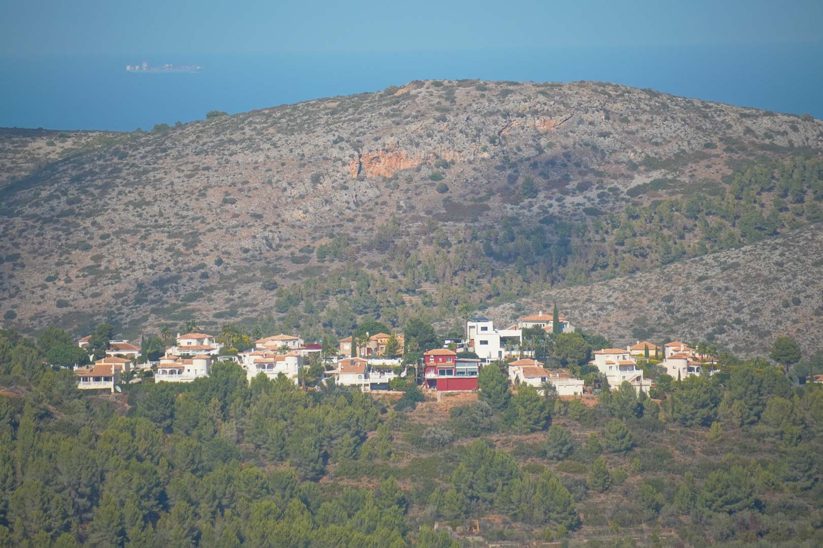 Panoramablick von der Immobilie auf die Siedlung am Hang, umgeben von Pinienwäldern, mit Blick auf die Berge und das Mittelmeer am Horizont.