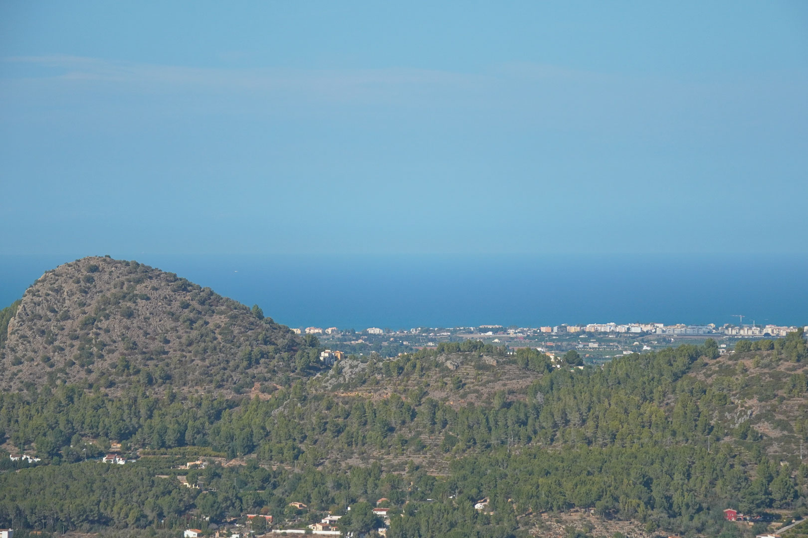 Panoramablick von der Immobilie auf mediterrane Bergketten, besiedelte Küstenstreifen und den blauen Horizont des Mittelmeers unter klarem Himmel.