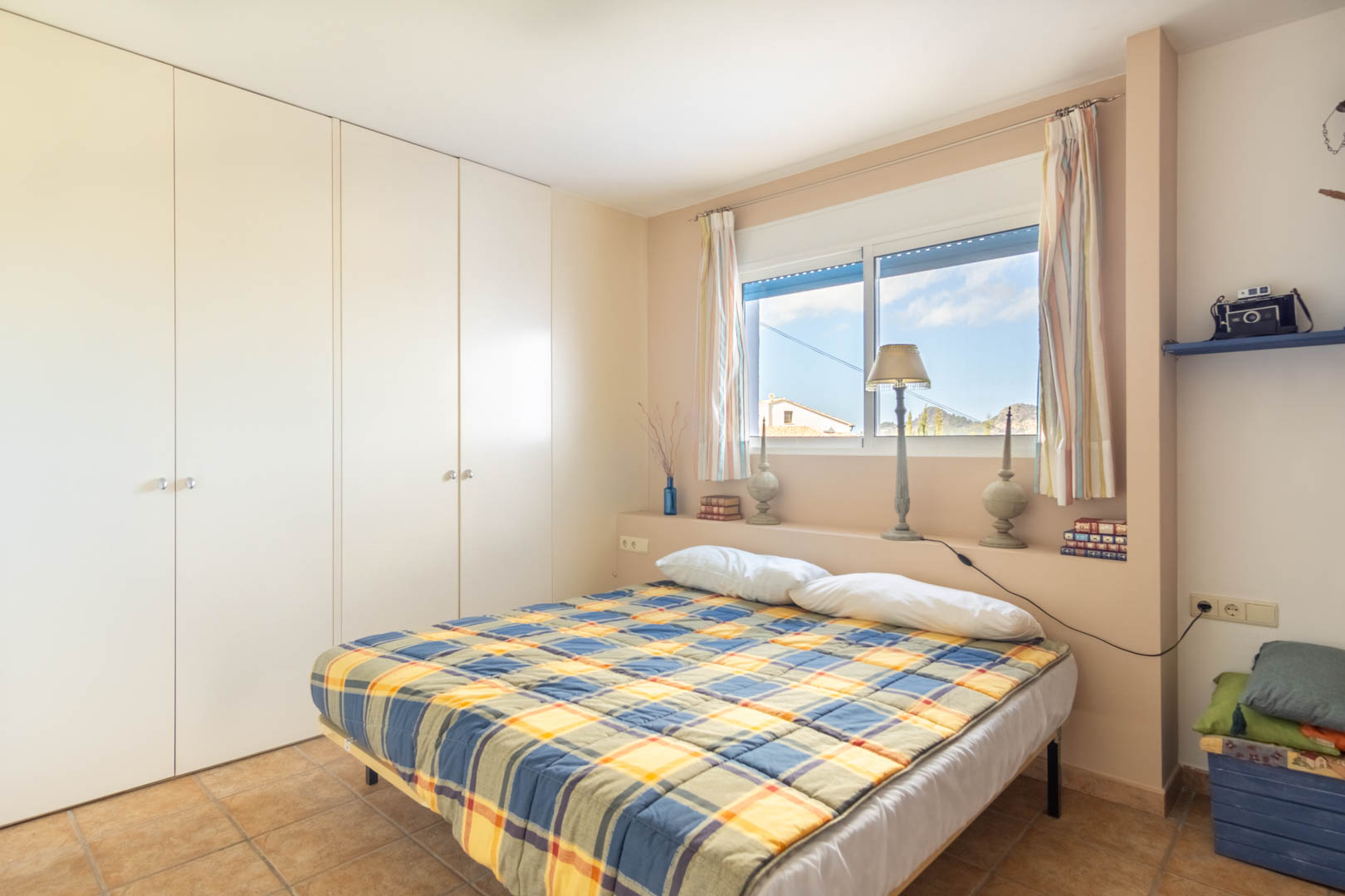 Schlafzimmer mit großen weißen Einbauschränken, rustikalem Fliesenboden und einem Fenster, das natürliches Licht und Bergblick bietet.