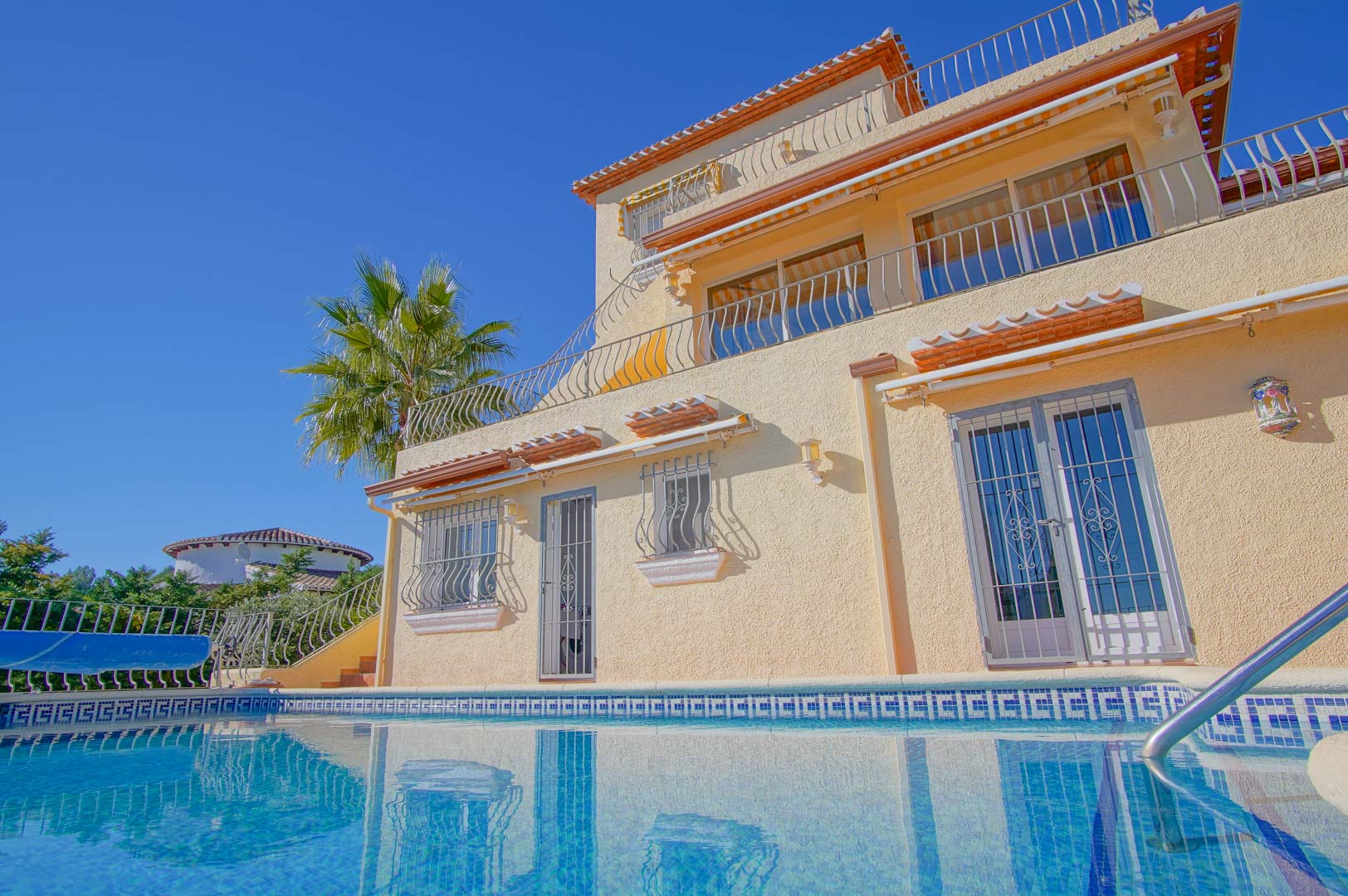 Außenansicht der dreistöckigen Villa vom Pool aus, mit abgestuften Terrassen, schmiedeeisernen Geländern und klassischer mediterraner Architektur.