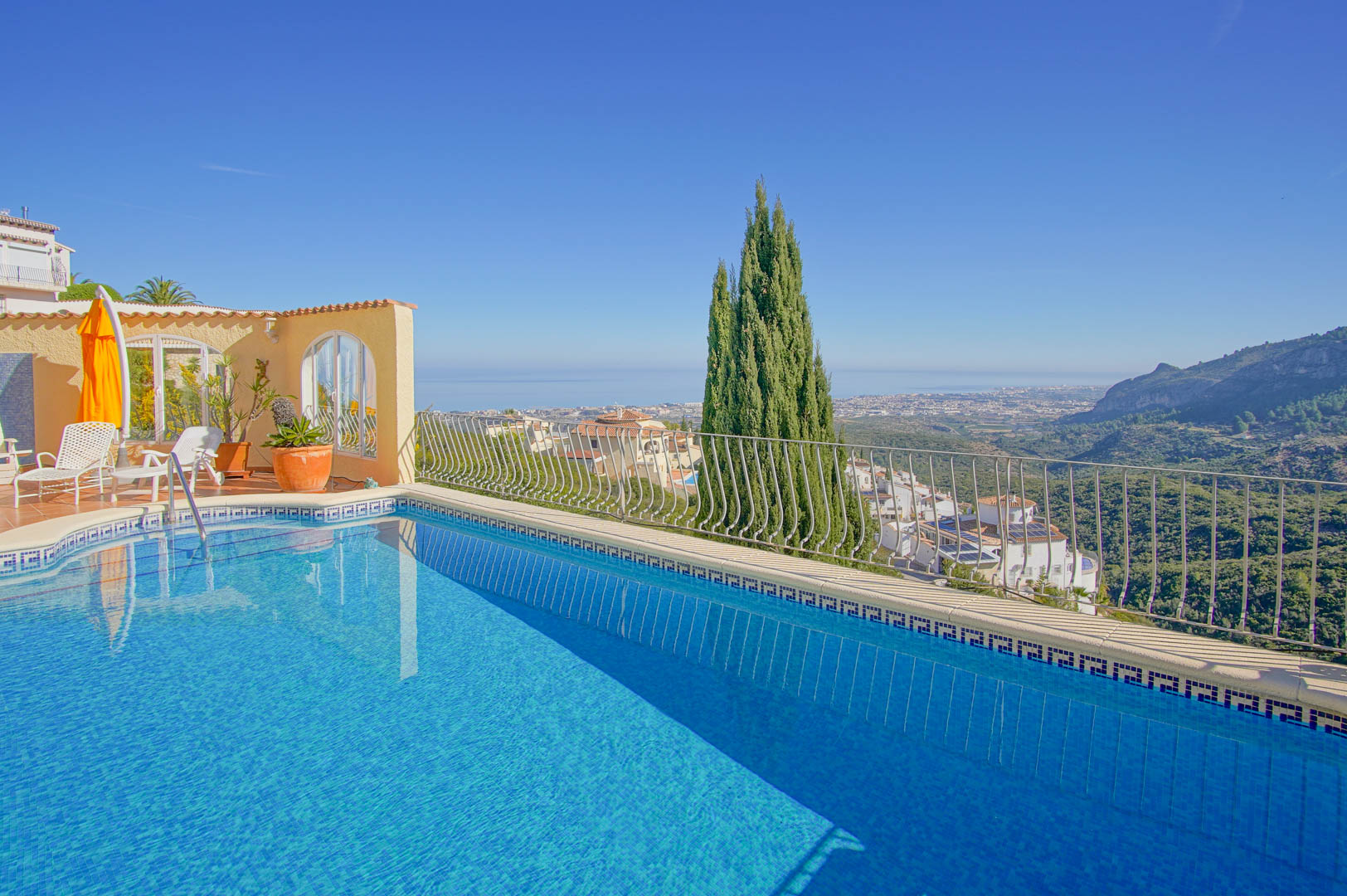 Außenpool mit blauen Mosaikfliesen und dekorativer Bordüre, angrenzend an eine Terrasse mit Panoramablick auf das Mittelmeer und die umliegende Berglandschaft.