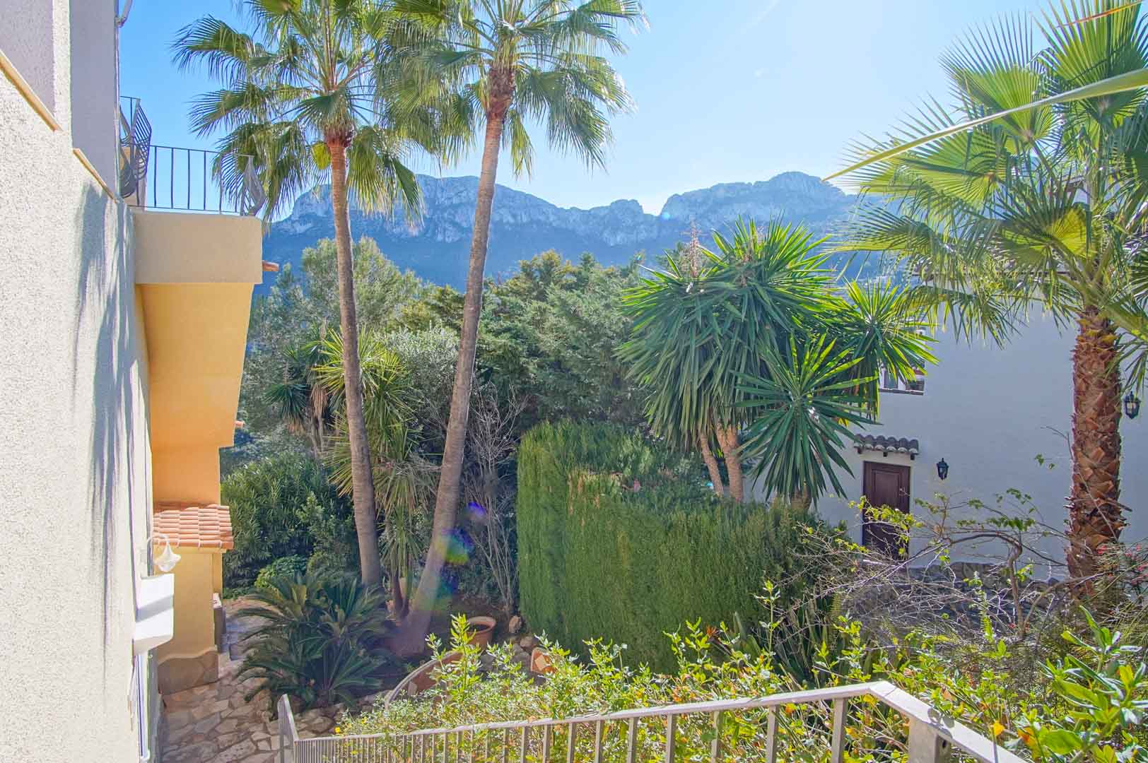Blick von der Außentreppe auf die Bergkette, umgeben von hochgewachsenen Palmen und einer üppigen mediterranen Gartenanlage.