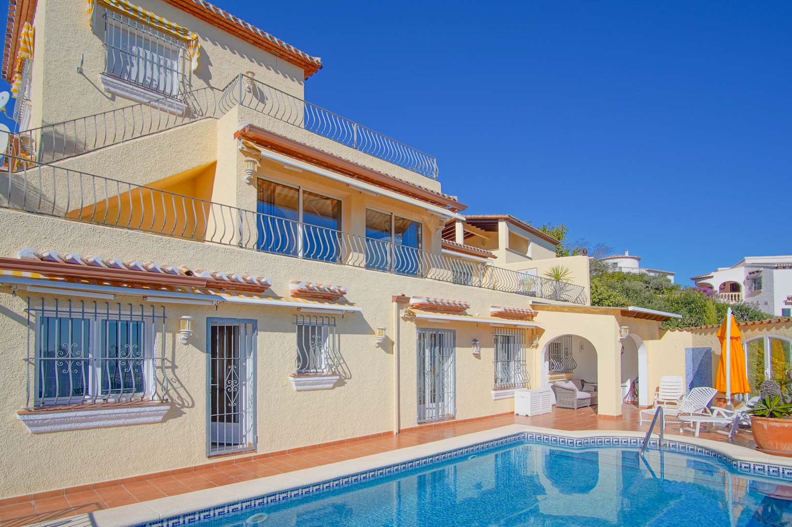 Dreistöckige Villa mit Mosaikpool, weitläufigen Terrassen mit schmiedeeisernen Geländern und einer sonnigen Poolterrasse aus Terrakotta-Fliesen.
