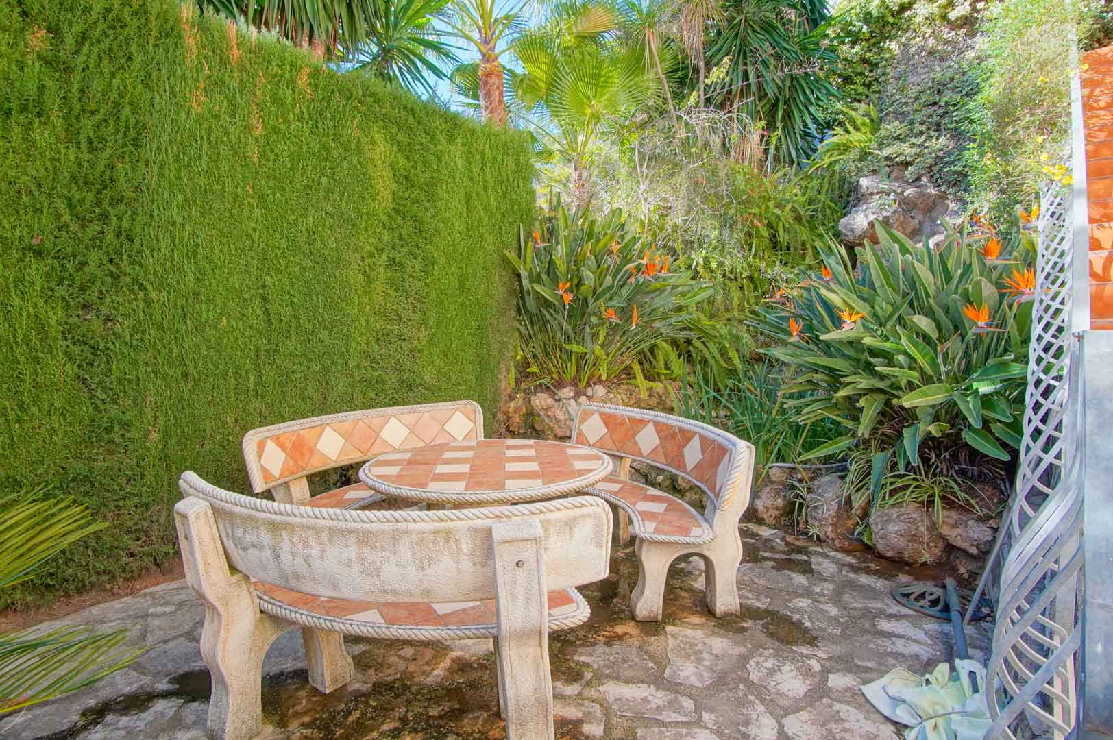 Ein privater Außenbereich mit Steintisch und geschwungenen Bänken mit Fliesendekor, umgeben von mediterraner Bepflanzung und Strelitzien.