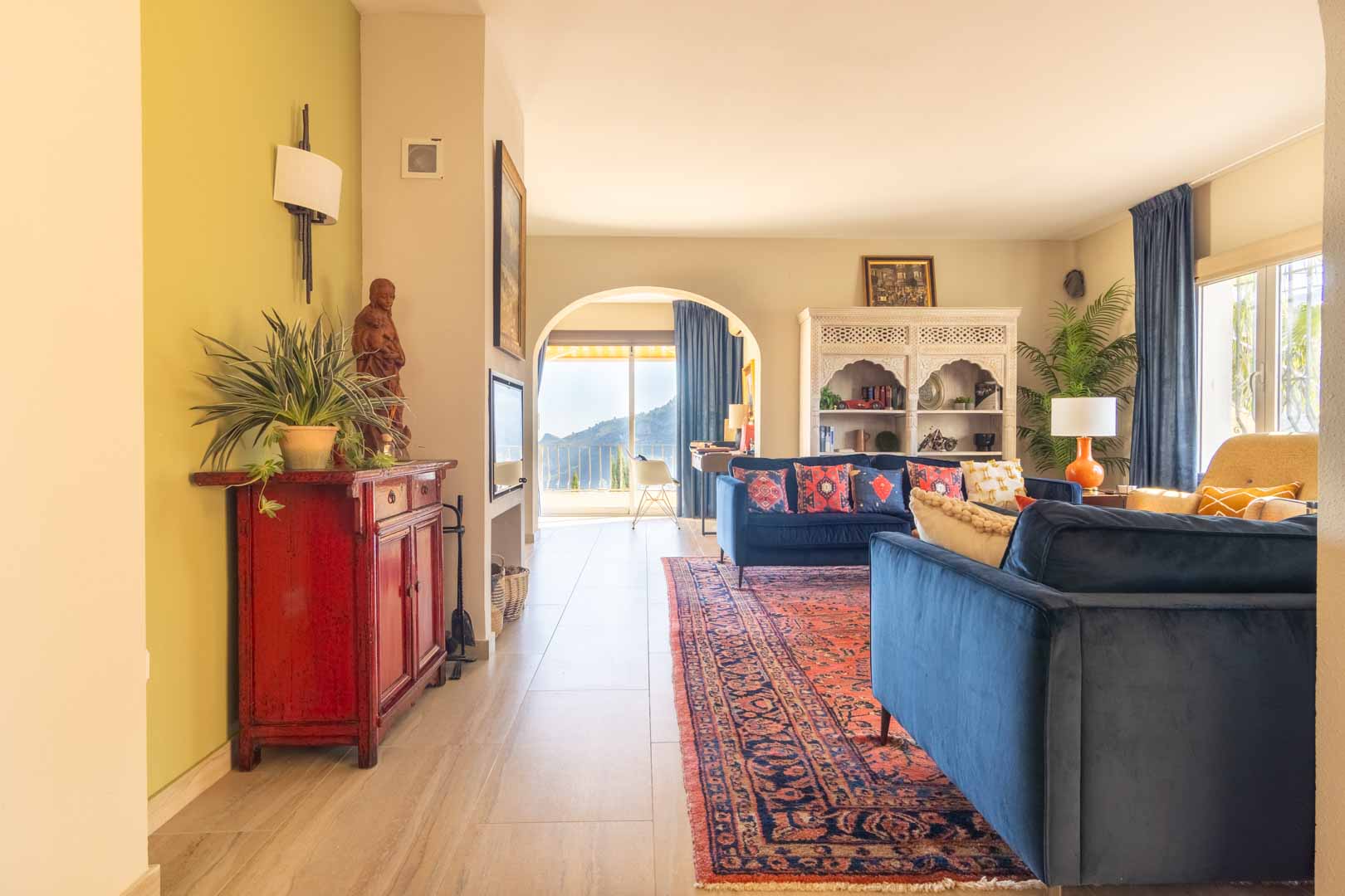 Helles Wohnzimmer mit blauen Samtsofas, Orientteppich und einem Rundbogen mit Bergblick. Ausgestattet mit geschnitzten Möbeln und hochwertigen Fliesenböden.