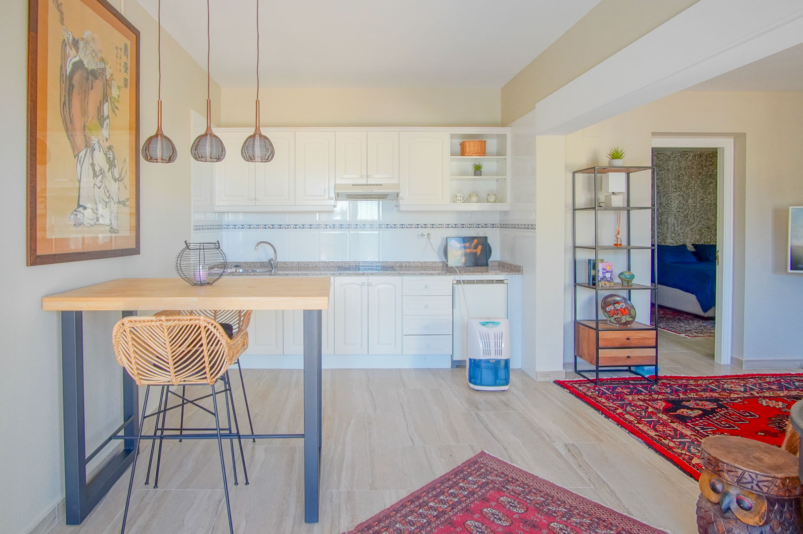 Offene Küche mit weißen Schränken, Granitarbeitsplatte und einem Frühstückstisch aus Holz. Der Raum ist mit orientalischen Teppichen und Kunstwerken gestaltet.