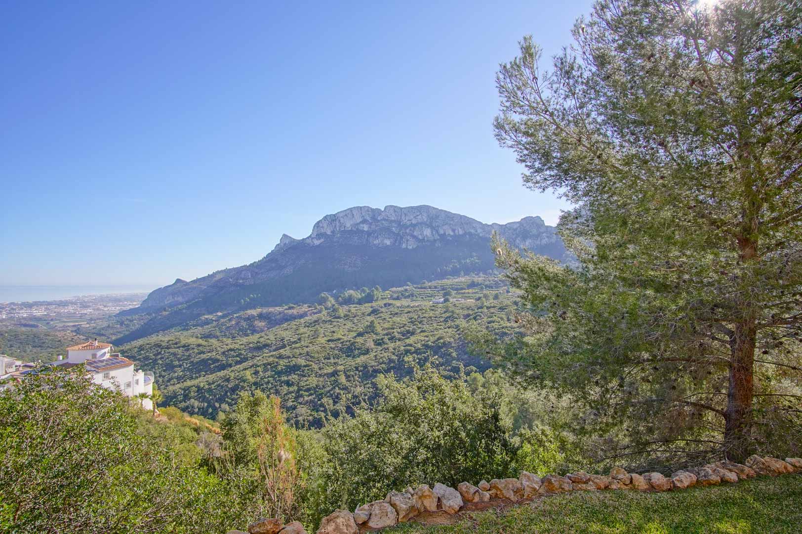 Panoramablick auf die Berge und das Tal vom Garten aus, mit einer Natursteinbegrenzung und Pinien, die den Blick auf die Mittelmeerküste freigeben.