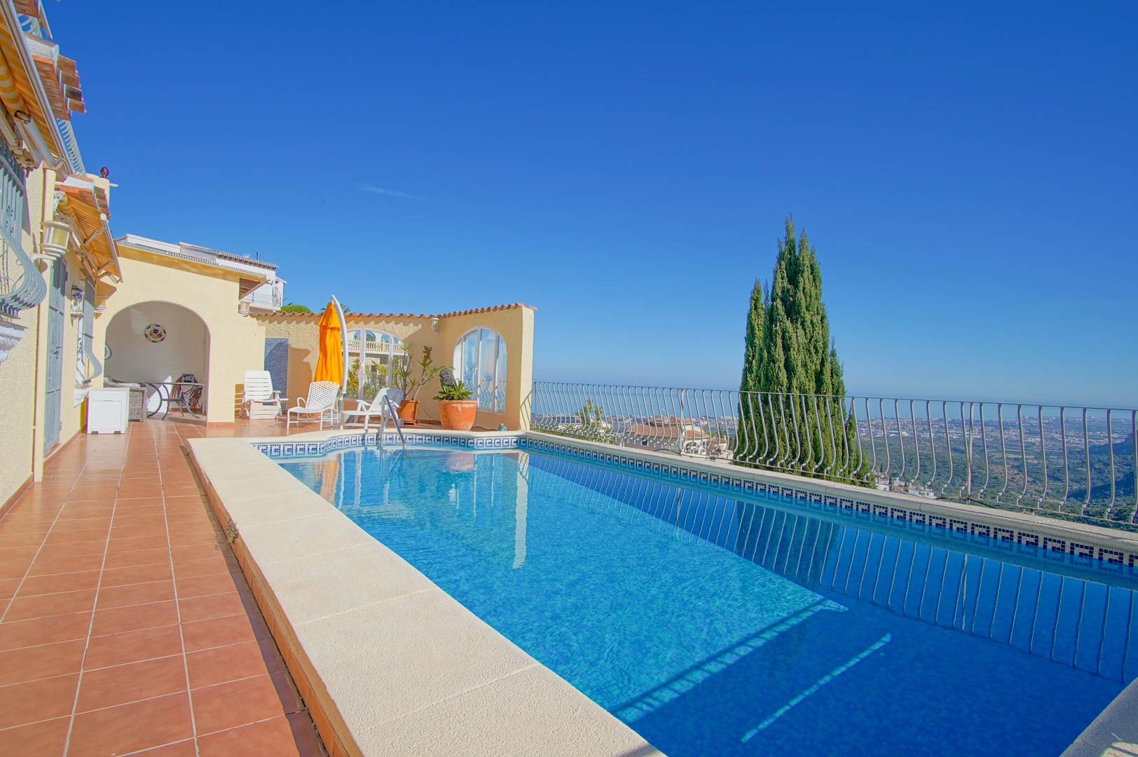 Rechteckiger Pool mit blauen Mosaikfliesen und griechischer Bordüre auf einer Terrakotta-Terrasse mit weitem Blick auf das Meer und Tal.
