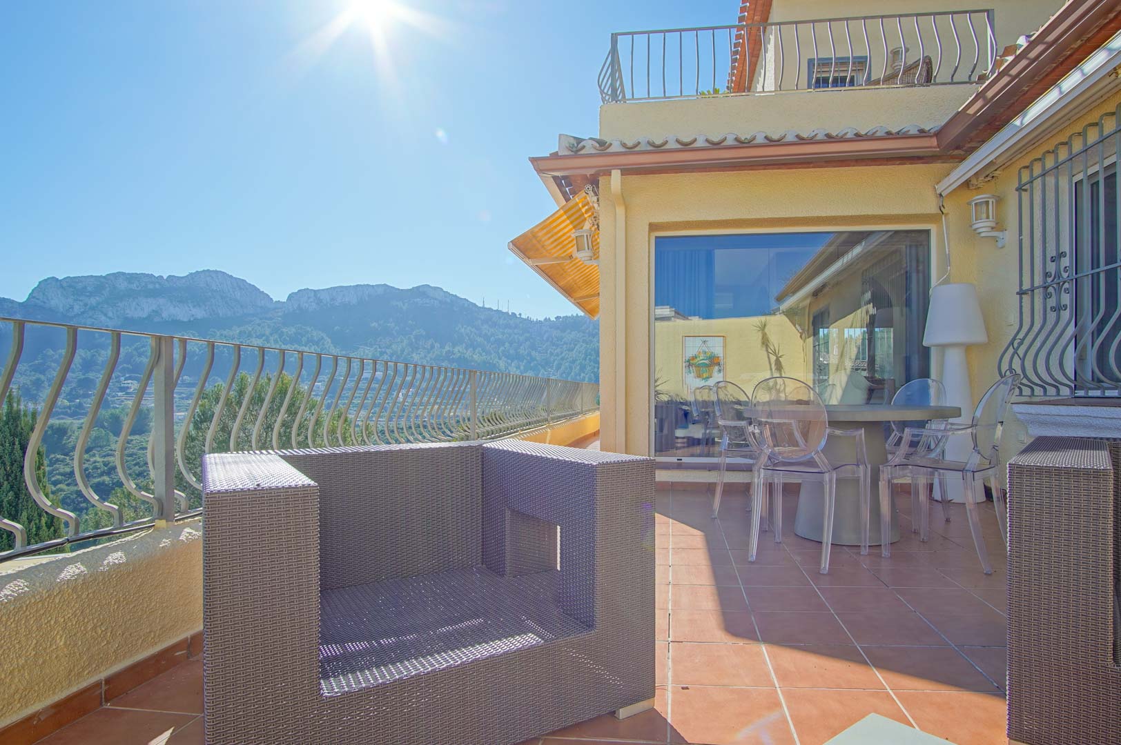 Terrasse mit Terrakottafliesen, Polyrattan-Sesseln und transparenten Stühlen, die einen weiten Blick auf die umliegende Berglandschaft bietet.