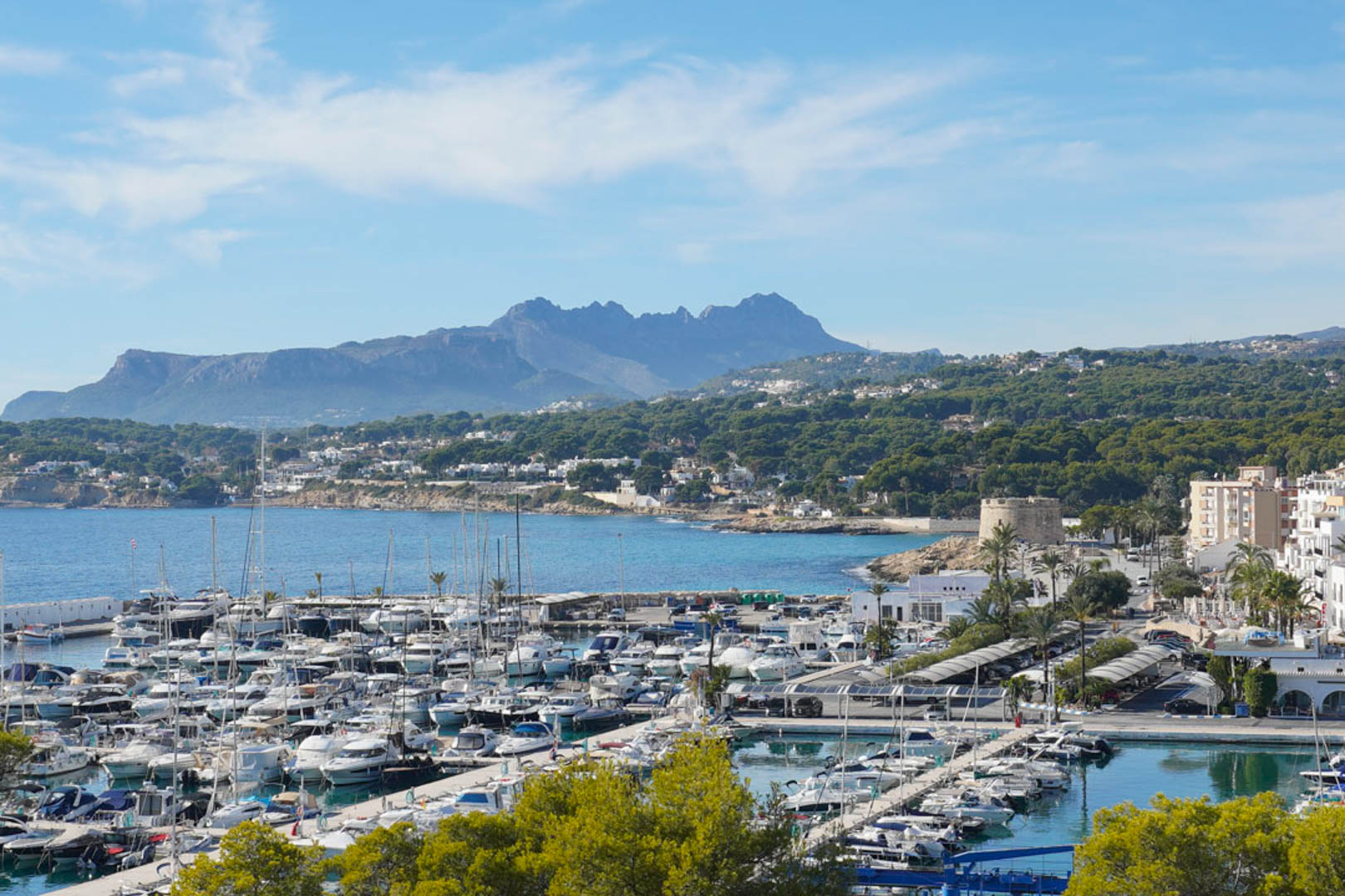 Panoramablick auf den Yachthafen von Moraira und die historische Festung, mit dem Bernia-Gebirge im Hintergrund an der Mittelmeerküste.
