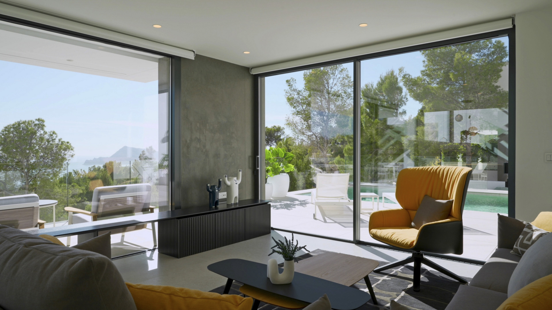 Heller Wohnbereich mit bodentiefen Glasfronten, Meer- und Poolblick. Ausgestattet mit Designmöbeln, einem senfgelben Sessel und direktem Zugang zur Terrasse.