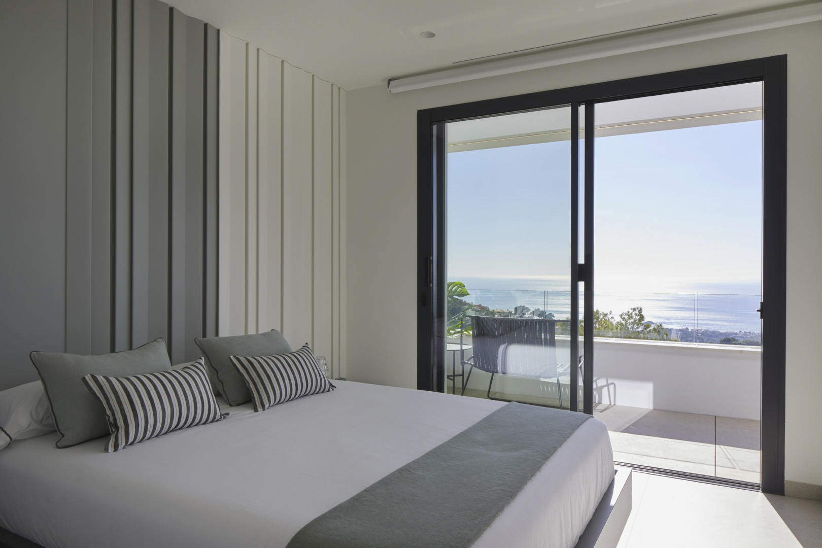 Helles Schlafzimmer mit dekorativer Wandvertäfelung und direktem Zugang zu einer privaten Terrasse mit Panoramablick auf das Mittelmeer.