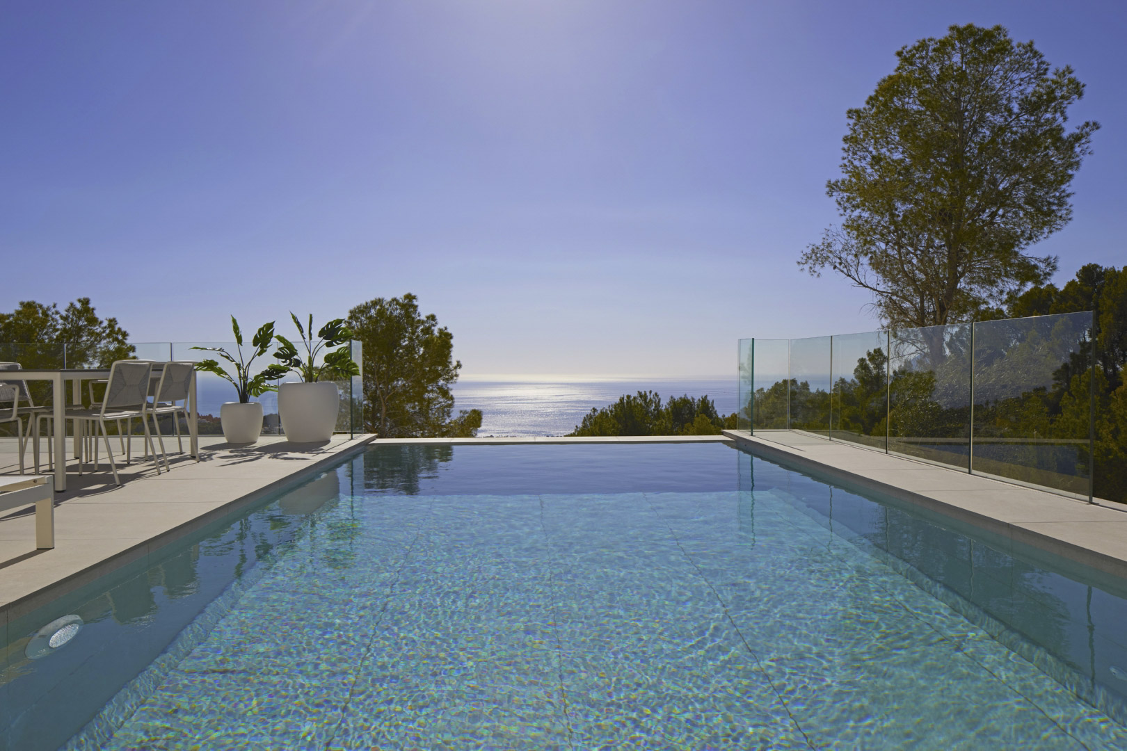 Infinity-Pool mit Panoramablick auf das Mittelmeer, umgeben von einer Fliesenterrasse mit modernen Außenmöbeln und rahmenlosen Glasgeländern.