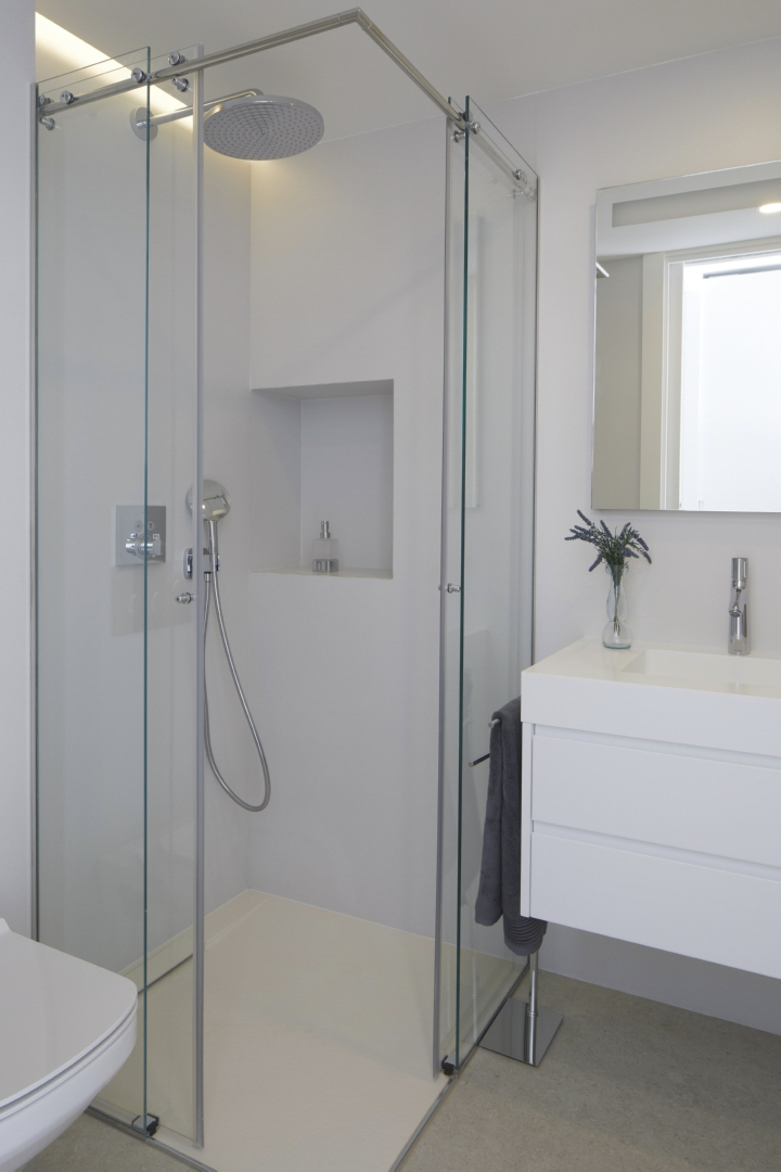 Modernes Badezimmer mit Glasduschkabine, Regenduschkopf und integrierter Wandnische. Schwebender weißer Waschtisch mit verchromten Armaturen und minimalistischem Design.