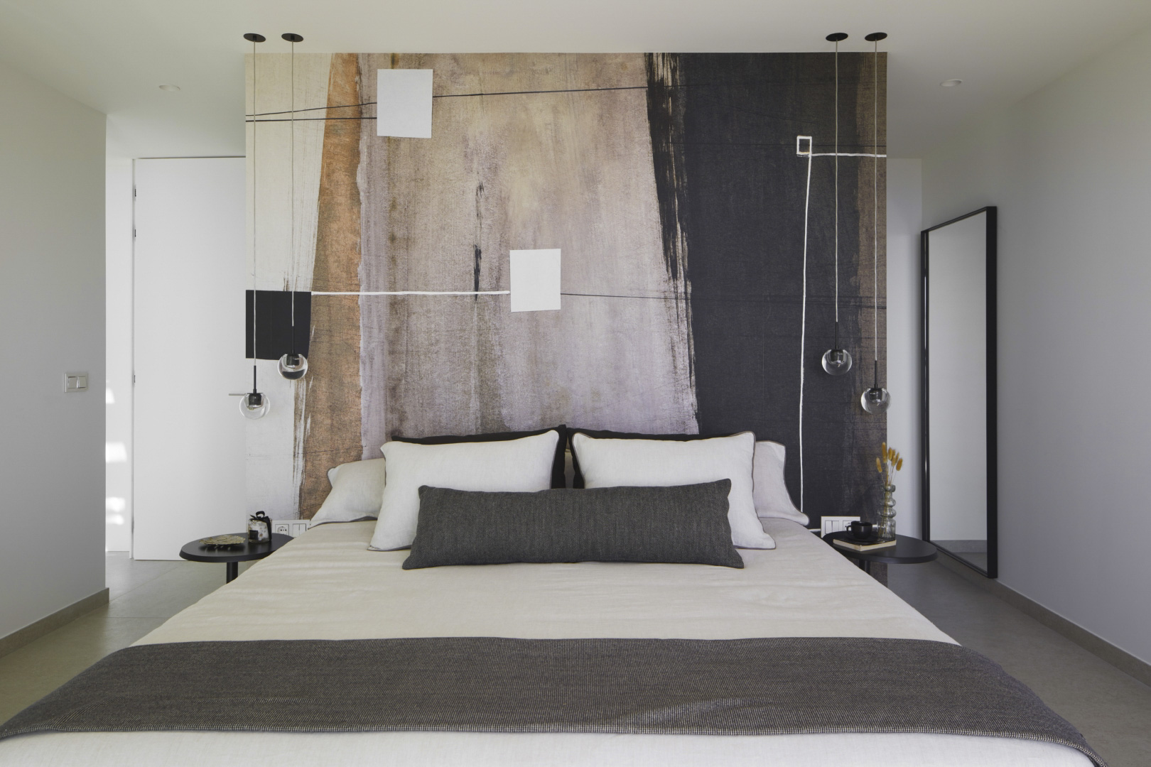 Modernes Schlafzimmer mit einem abstrakten Wandbild hinter dem Bett, minimalistischen Pendelleuchten und schlichten schwarzen Nachttischen.