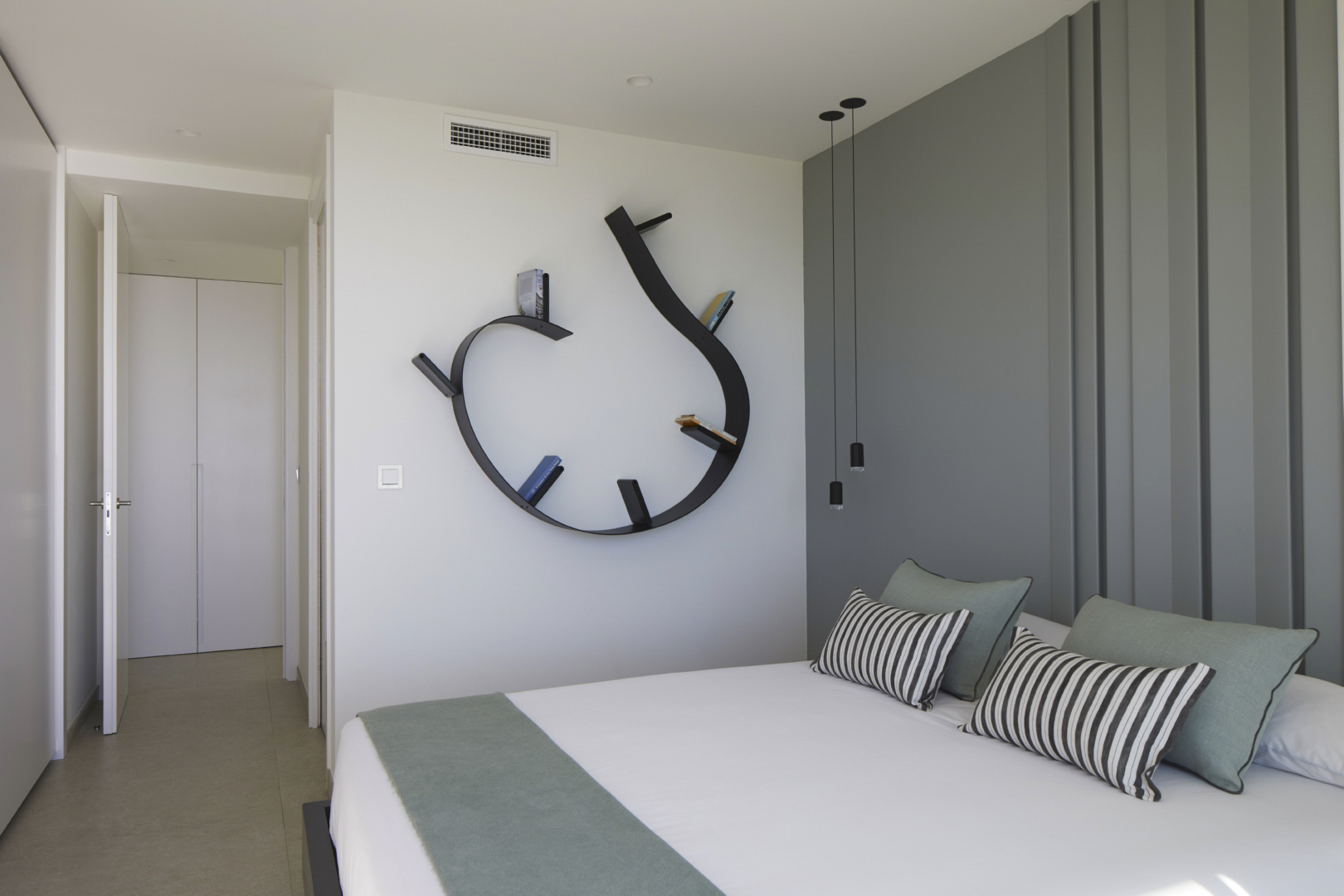 Modernes Schlafzimmer mit einem markanten geschwungenen schwarzen Wandregal, grauer Akzentwand in Paneel-Optik und minimalistischen Pendelleuchten.