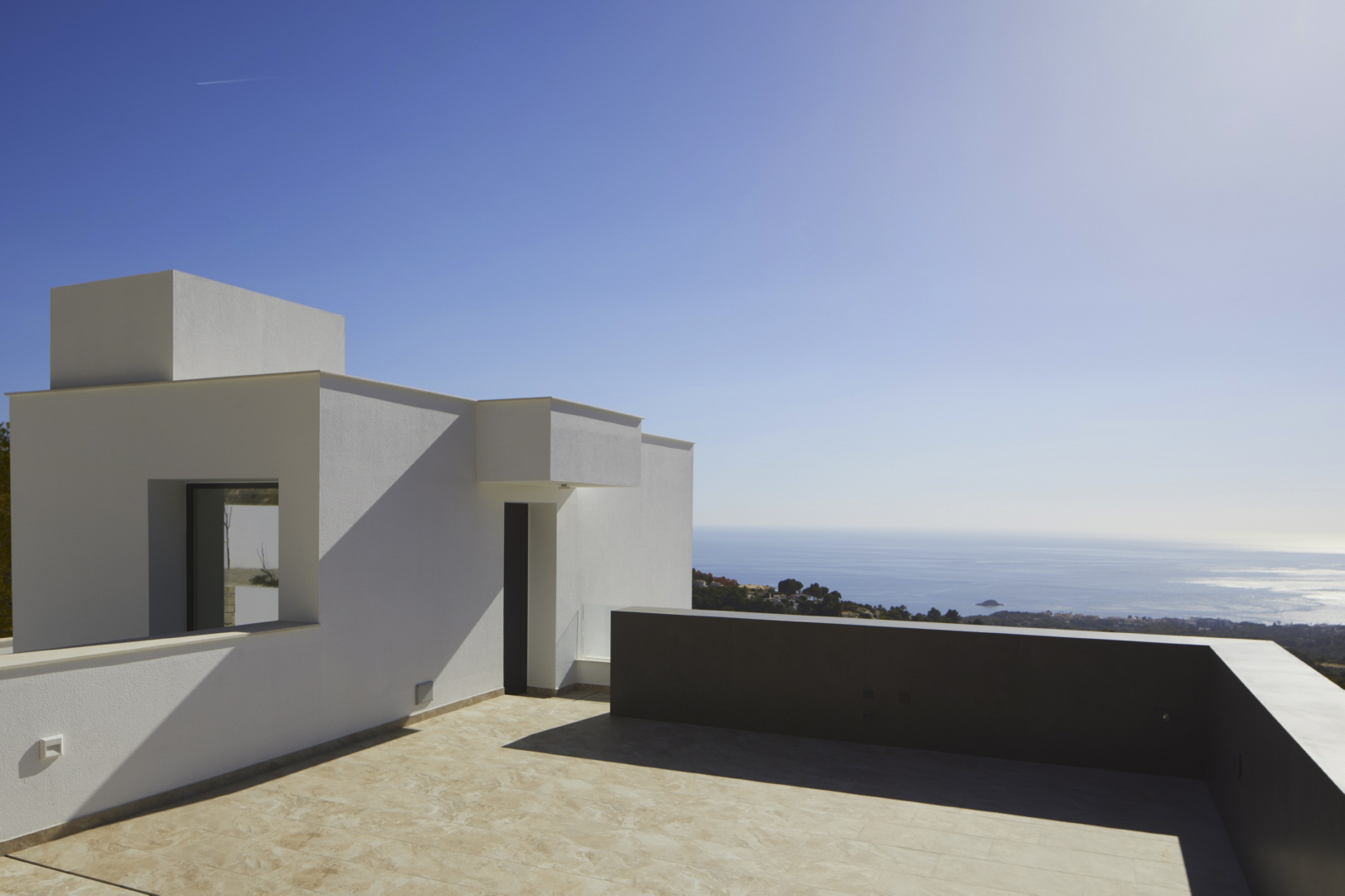 Obere Terrasse mit minimalistischer weißer Architektur, Fliesen in Steinoptik und weitem Panoramablick auf das Mittelmeer.