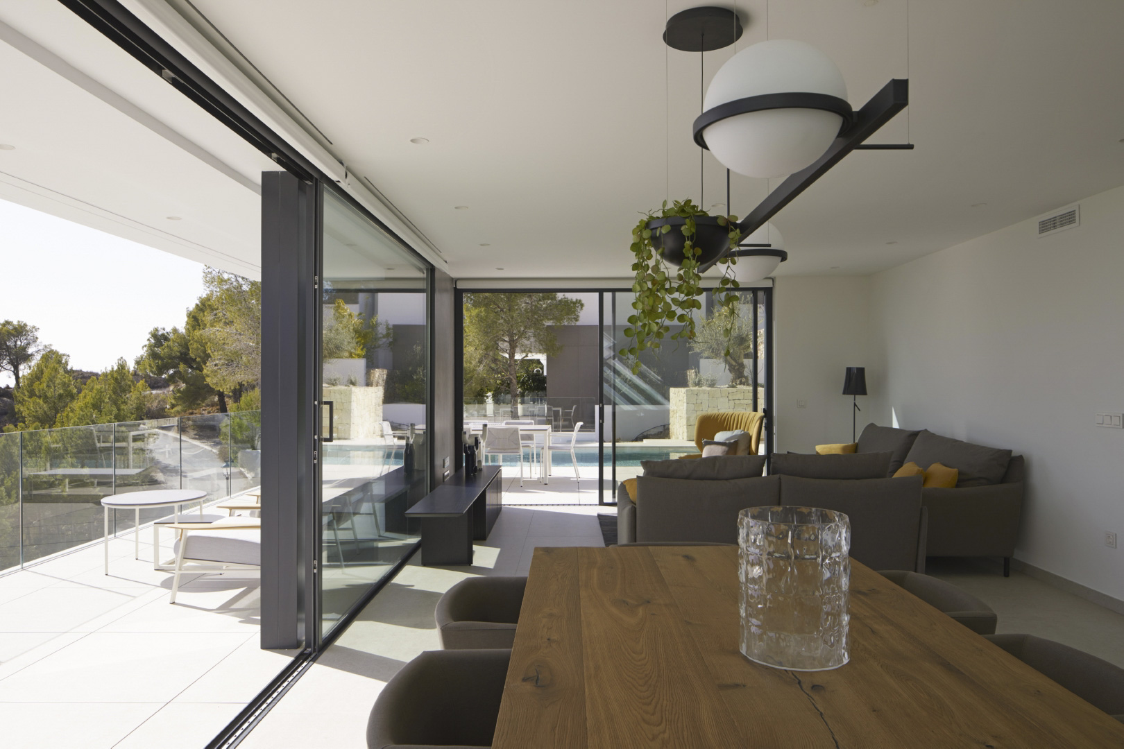 Offener Wohn- und Essbereich mit massivem Holztisch, modernen Pendelleuchten und großen Glasschiebetüren, die direkten Zugang zur Terrasse und zum Pool bieten.