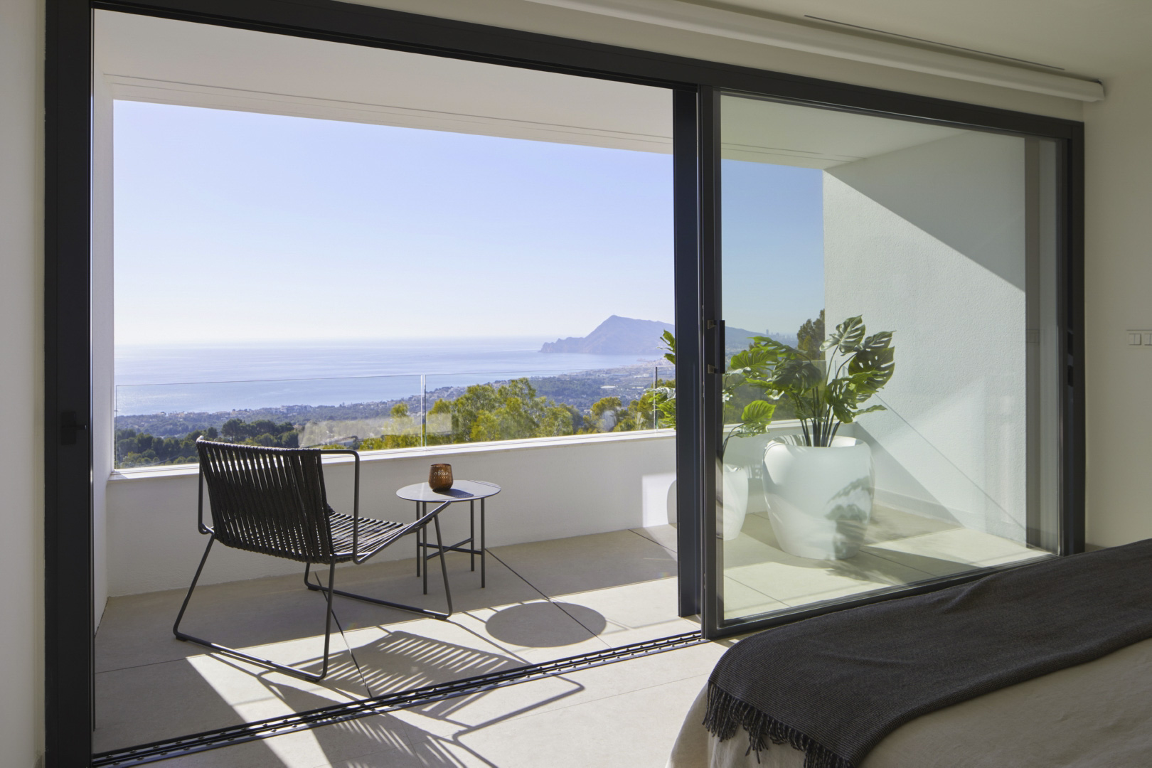 Schlafzimmer mit großen Glasschiebetüren zur privaten Terrasse. Mit Panoramablick auf das Mittelmeer, modernen Außenmöbeln und einem Glasgeländer.