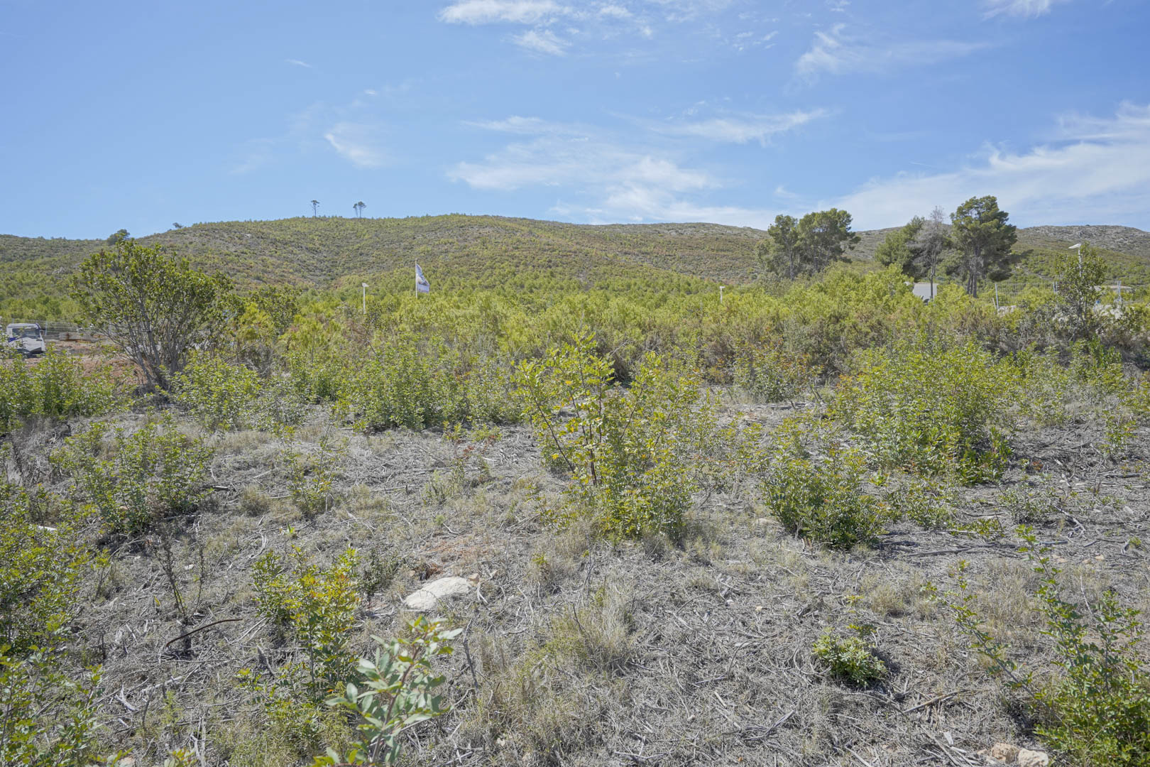 Ein 1514 m2 großes Baugrundstück mit natürlicher mediterraner Vegetation und weitem Blick auf die umliegenden Hügel unter blauem Himmel.
