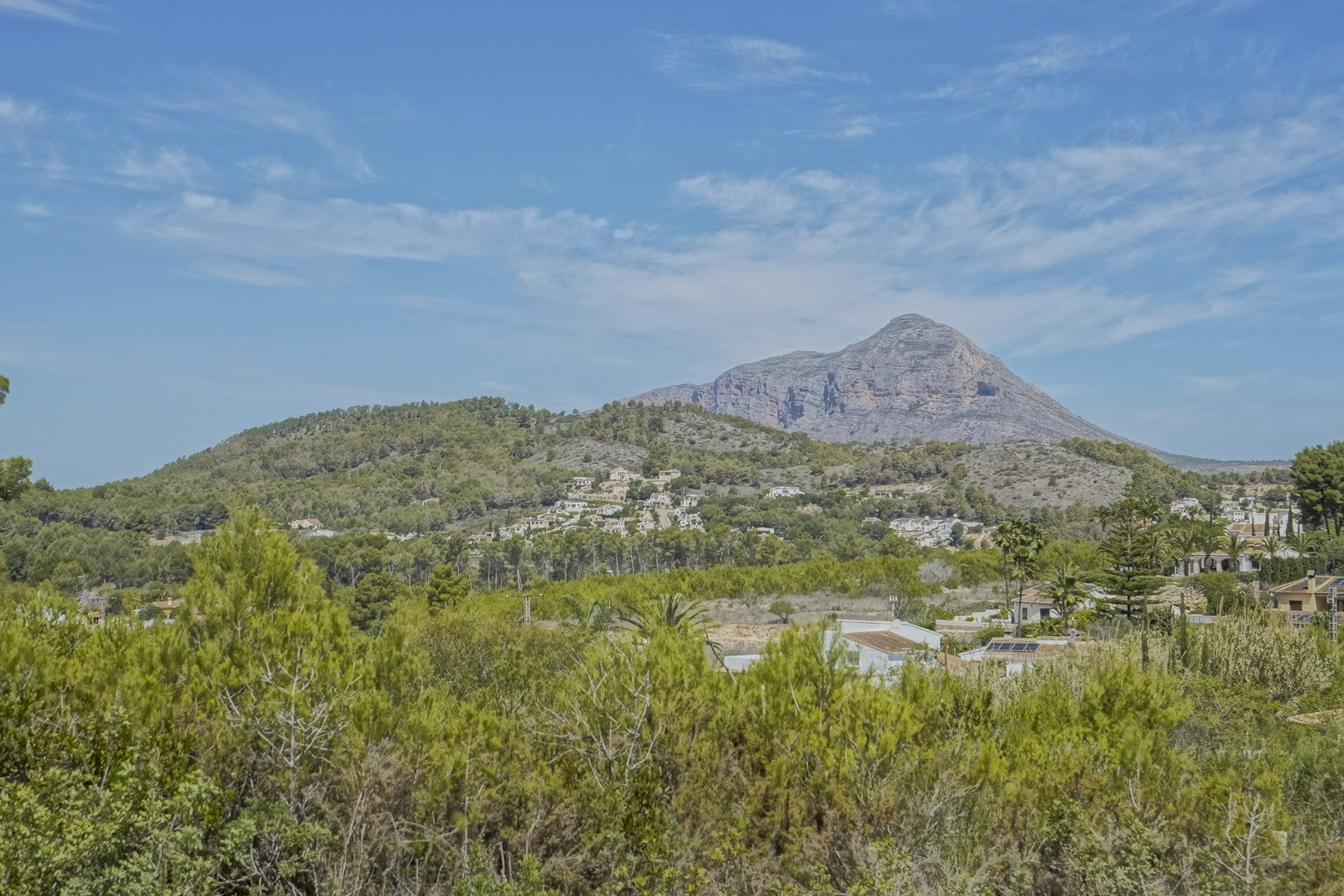 Panoramablick auf das Montgó-Massiv und die umliegende mediterrane Landschaft mit Pinienwäldern und sanften Hügeln unter strahlend blauem Himmel.