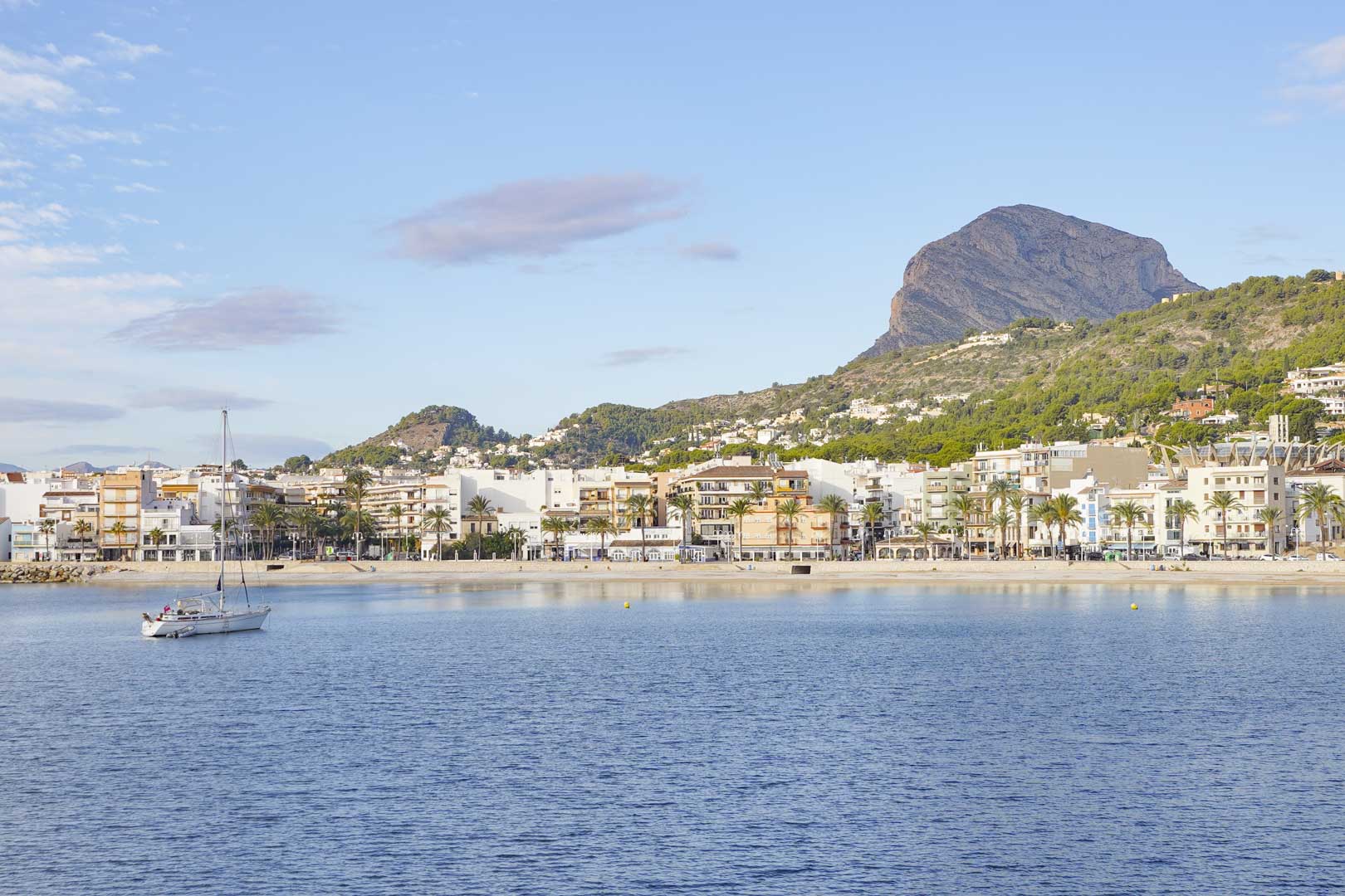 Panoramablick auf die Bucht von Jávea mit dem majestätischen Berg Montgó im Hintergrund und einem Segelboot auf dem ruhigen Mittelmeer.