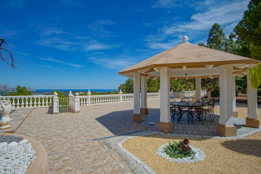 Außenpavillon mit weißen Säulen und schmiedeeisernen Möbeln auf einer gefliesten Terrasse mit weitem Blick auf das Mittelmeer.