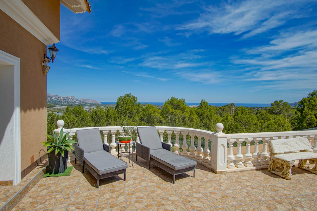Erhöhte Terrasse mit Natursteinboden, weißer Balustrade und grauen Sonnenliegen, die einen Panoramablick auf den Pinienwald und das Mittelmeer bietet.