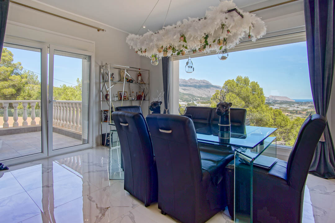 Formelles Esszimmer mit Marmorboden, Glastisch und schwarzen Lederstühlen, mit weitem Panoramablick auf die Berge und das Meer durch große Fensterfronten.