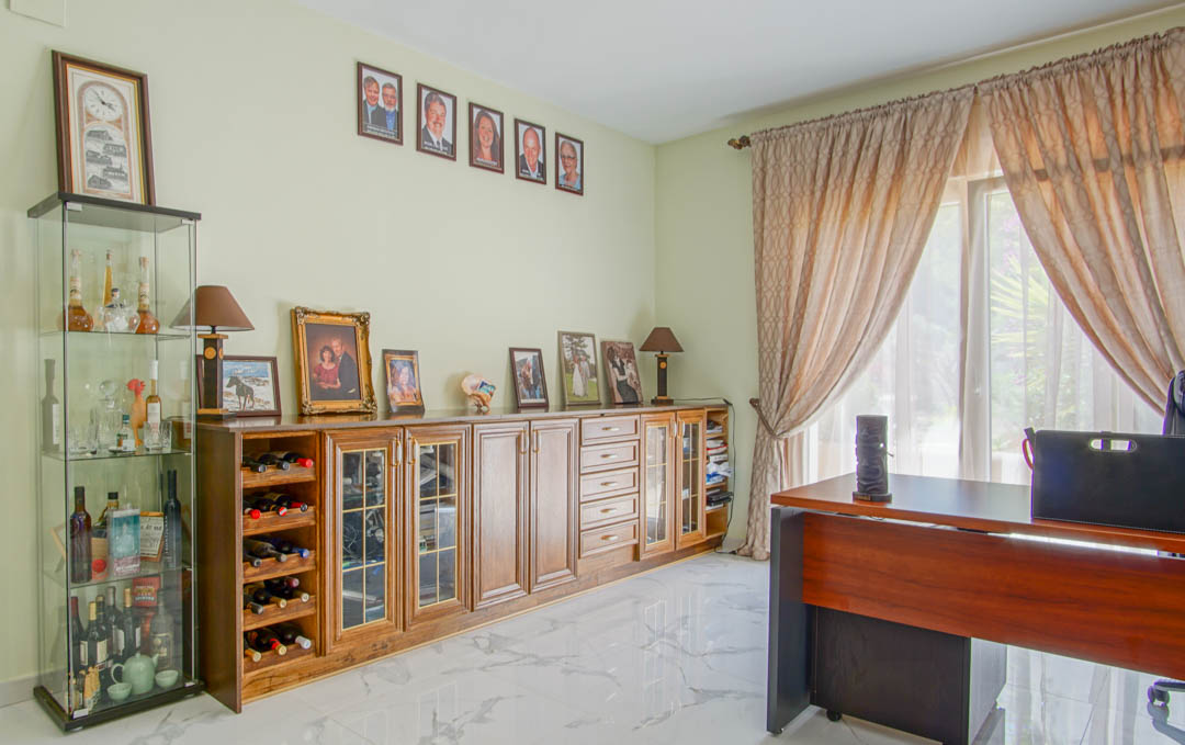 Helles Arbeitszimmer mit Marmorboden, Holzschreibtisch und einem großen Sideboard mit integriertem Weinregal und Vitrinenschränken.