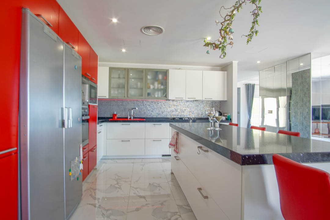 Moderne Designerküche mit rot-weißen Hochglanzfronten, einer großzügigen Kochinsel und hochwertigem Bodenbelag in edler Marmoroptik.