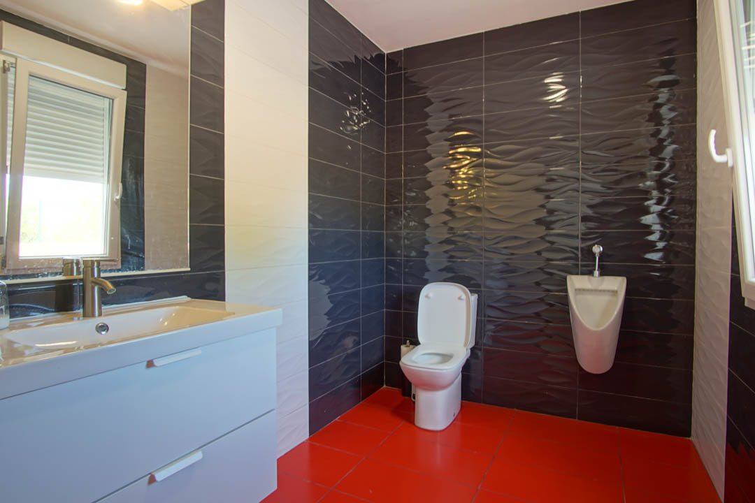 Modernes Badezimmer mit roten Bodenfliesen, dunkel gewellten Wandfliesen, einem weißen Waschtisch und einem wandmontierten Urinal.