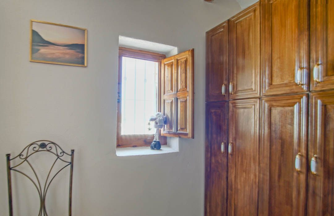 Rustikaler Raum mit massivem Holzeinbauschrank, traditionellem Fenster mit Holzläden und einem dekorativen Schmiedeeisenstuhl.