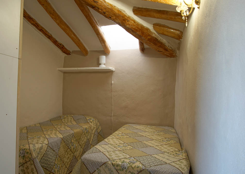Rustikales Schlafzimmer mit Dachschrägen, sichtbaren Holzbalken und einem Dachfenster. Der Raum bietet zwei Einzelbetten und Wände mit traditionellem Putz.