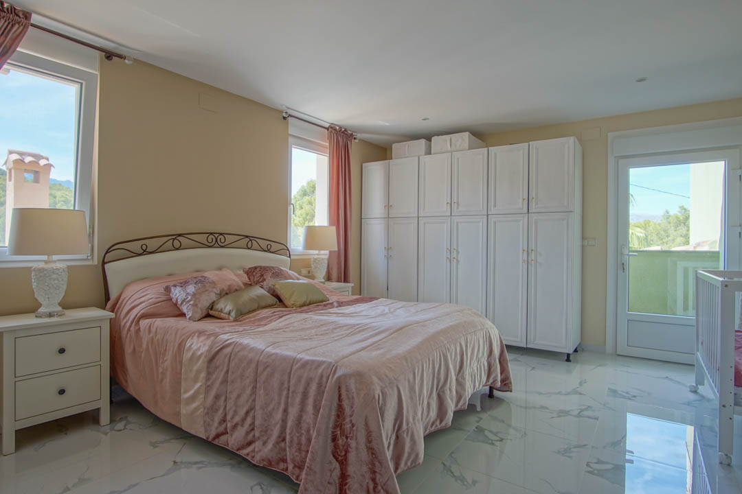 Schlafzimmer mit Feinsteinzeug in Marmoroptik, großen weißen Schränken und Balkonzugang mit Blick auf die umliegende Berglandschaft.