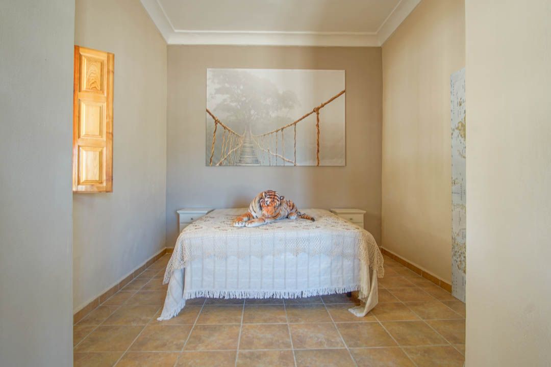 Schlafzimmer mit Keramikfliesenboden, Doppelbett zwischen weißen Nachttischen und einem Fenster mit traditionellen Holzfensterläden.