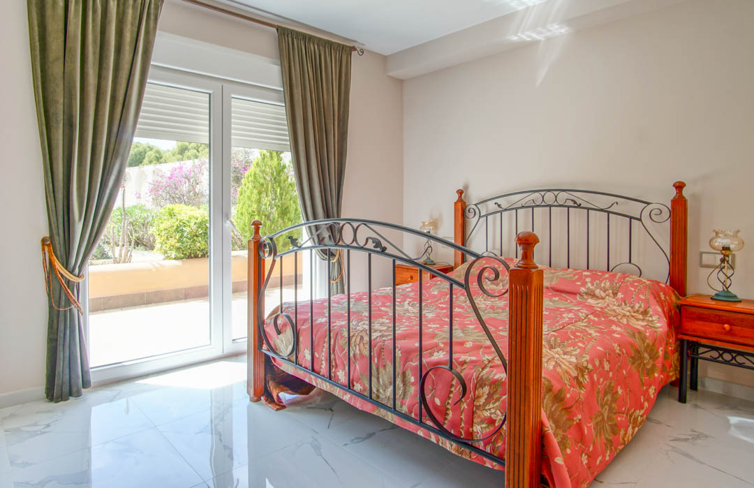 Schlafzimmer mit poliertem Marmorboden, einem Bettgestell aus Schmiedeeisen und Holz sowie direktem Zugang zur Terrasse durch große Glastüren.