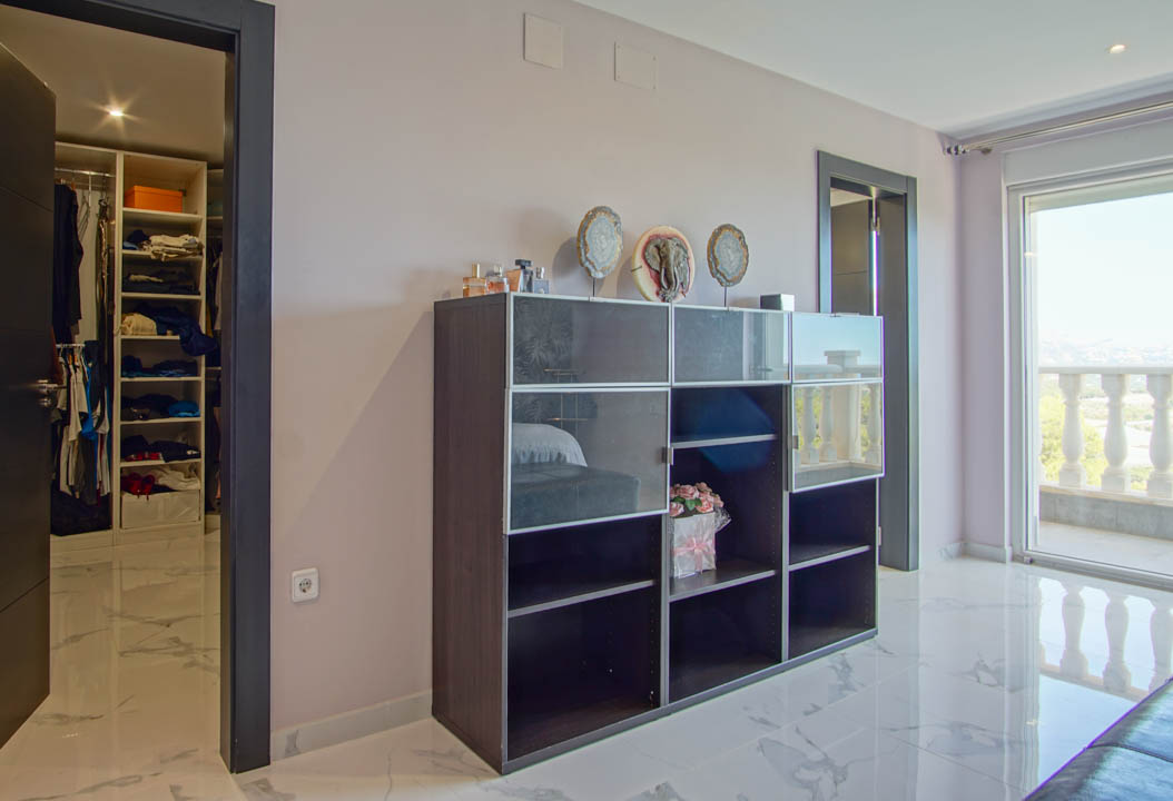 Schlafzimmer mit weißem Marmorboden, begehbarem Kleiderschrank und Zugang zum Balkon mit einer klassischen Steinbalustrade.
