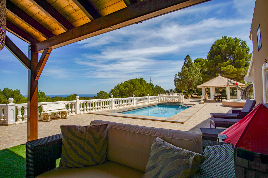 Terrasse mit Pool, weißer Balustrade und Panoramameerblick. Mit Loungebereich unter einer Holzpergola und einem Pavillon inmitten mediterraner Pinien.