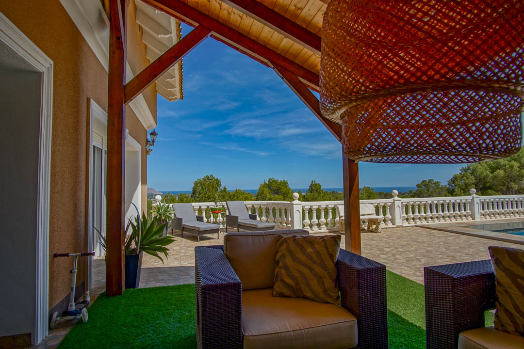 Überdachte Terrasse mit Holzbalken und Sitzbereich, die einen Panoramablick auf das Mittelmeer hinter einer klassischen weißen Balustrade bietet.