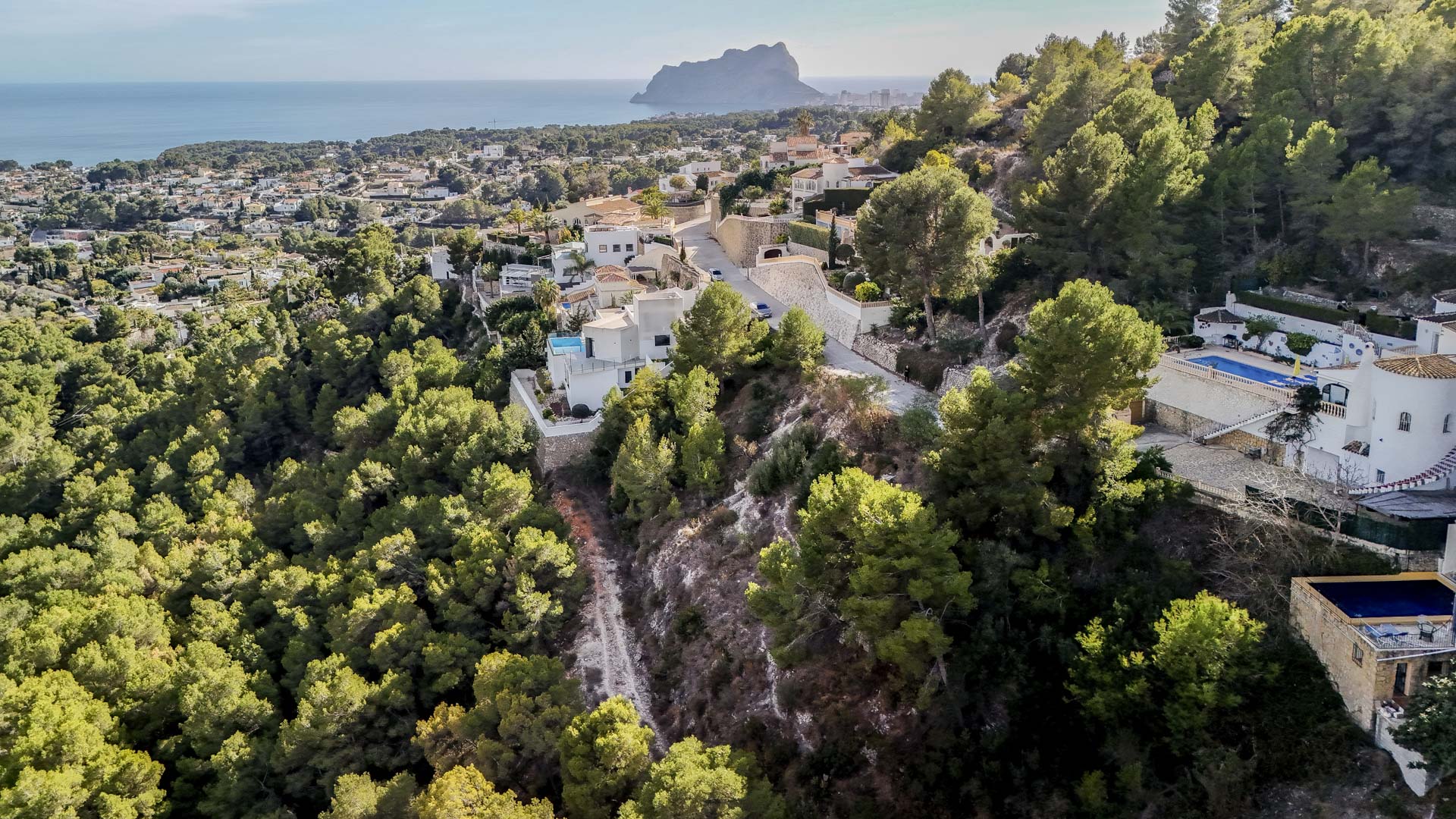 Luftaufnahme des Wohngebiets in Benissa mit Blick auf den Peñón de Ifach und die weitläufige geschützte Grünzone, die die Grundstücke umgibt.